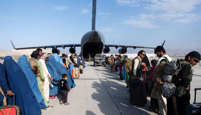 افغانستان سے نکلنے کے خواہاں افغان باشندے فوجی طیارے میں سوار ہونے کے لیے قطار میں کھڑے ہیں— فوٹو: اے ایف پی