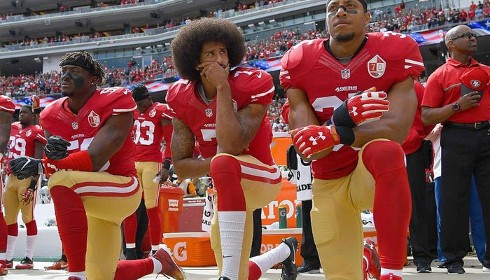 سب سے پہلے امریکی فٹبال کولن کائپر نک (درمیان) نے 2016 میں گھٹنوں پر بیٹھ کر نسل پرستی کیخلاف احتجاج ریکارڈ کرانا شروع کیا— فوٹو: بی بی سی
